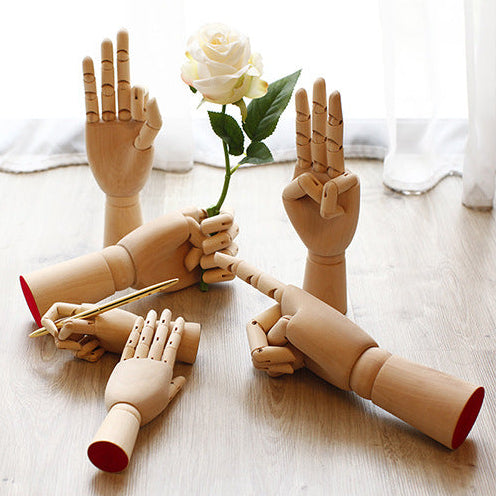 Wooden mannequin hands with a white rose on a light wooden surface.
